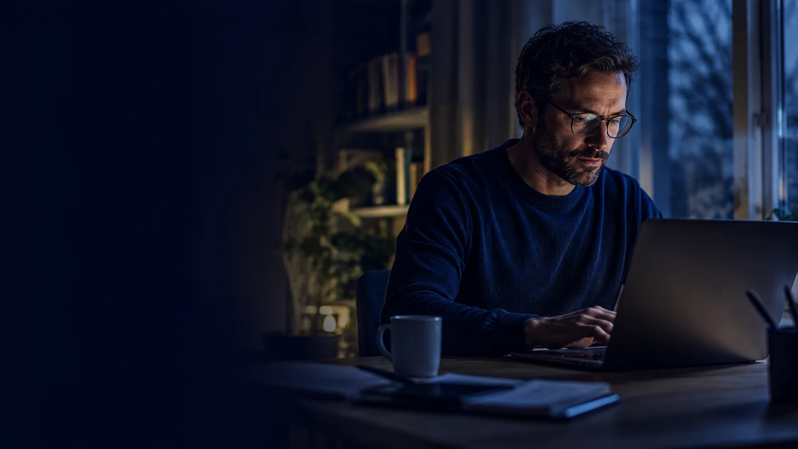 Profissional trabalhando à noite no notebook, iluminado pela tela